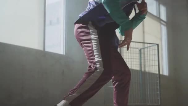 Experienced young hip-hop street dancer performing in front of large window in the dark abandoned building. The man making moves, jumping and crouches dancing.. Slow motion - Materiaali, video