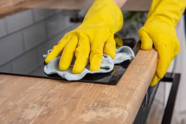 Joven mujer manos limpieza de una moderna placa de inducción negro por un trapo, tareas domésticas
 - Foto, Imagen