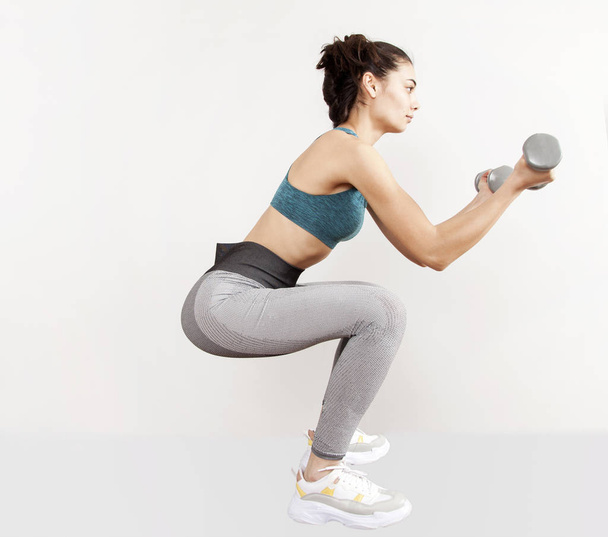 Sporty woman does the exercises with dumbbells on gray background. - Photo, Image
