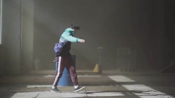 Young asian hip-hop male dancer in sport wear dancing in the dark abandoned building in front of blue gas barrel. Contemporary. Hip hop culture. Rehearsal. Slow motion. - Video, Çekim
