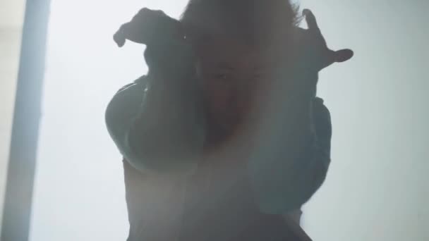 Portré, fiatal ázsiai hip-hop táncos férfi énekel a nagy ablakon keresztül elhagyott épület keres, a kamera közelről. Az ember kezét csavaró, ugrás, és körül forog. Lassú mozgás. - Felvétel, videó