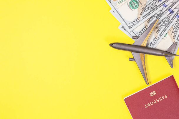 One hundred dollar bills, airplane, headphones, foreign passport on bright yellow paper background. Copy space. Travel and budget trip concept, flat lay. Hand luggage, minimalism, frame of objects.on bright yellow paper background. Copy space.  - Foto, Bild