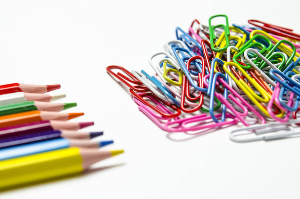 Many multi-colored stationery clips for documents and multi-colored pencils lie on a white background - Foto, Bild