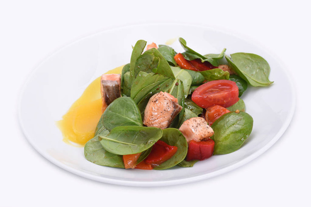 Salade délicieuse et saine - poisson rouge et légumes verts (épinards, tomates, paprika) avec sauce sur une assiette blanche
 - Photo, image