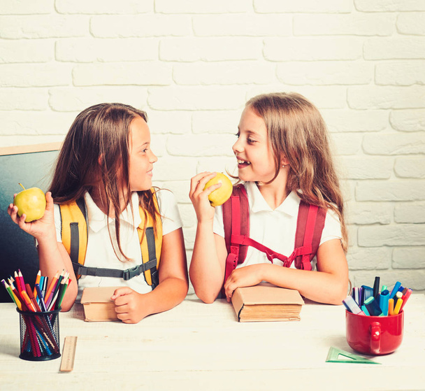 Back to school and home schooling. Little girls eat apple at lunch break. School time of girls. Friendship of small sisters in classroom at knowledge day. Happy school kids at lesson in september 1 - Fotoğraf, Görsel
