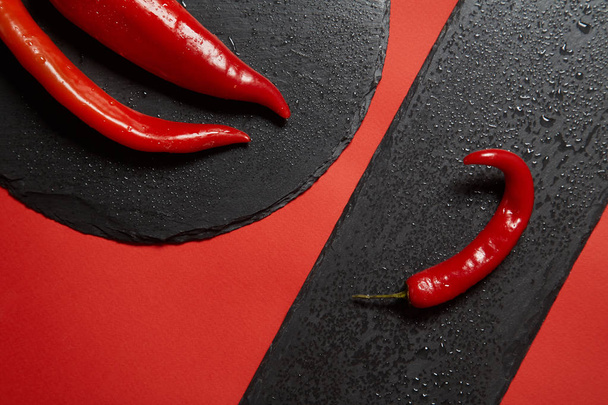 Red hot chili pepper and red peppper on a black slate dish on a red background. - Φωτογραφία, εικόνα