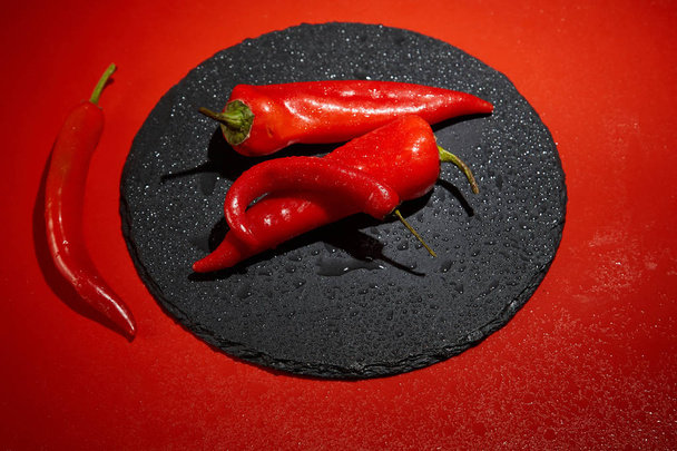 Red hot chili pepper and red peppper on a black slate dish on a red background. Image. - Φωτογραφία, εικόνα
