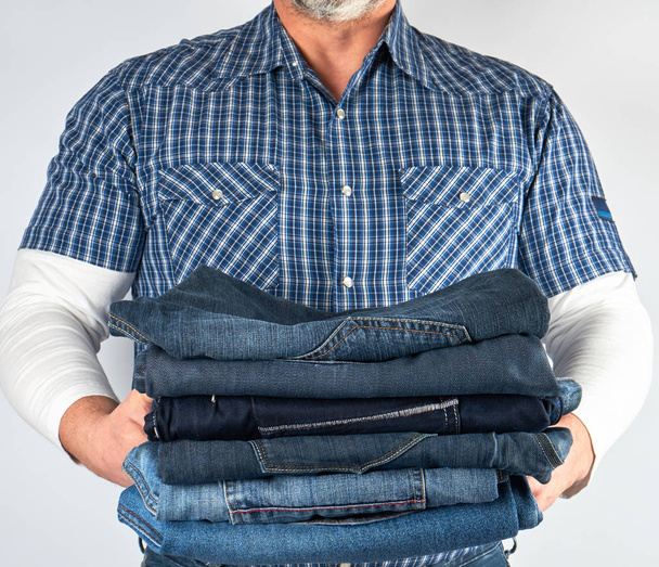 homem de jeans e camisa xadrez azul segurando uma pilha de jeans
 - Foto, Imagem