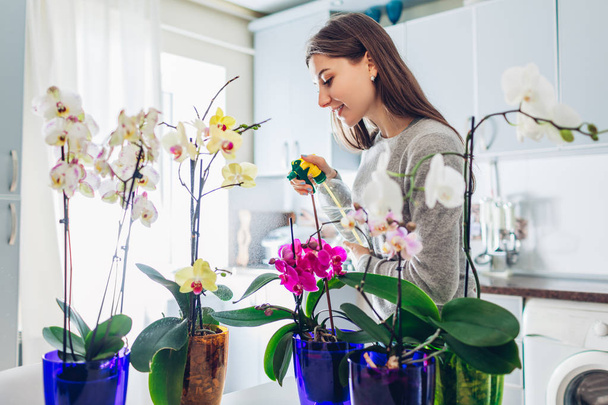 Frau sprüht Wasser auf Orchideen in der Küche. Hausfrau kümmert sich um heimische Pflanzen - Foto, Bild