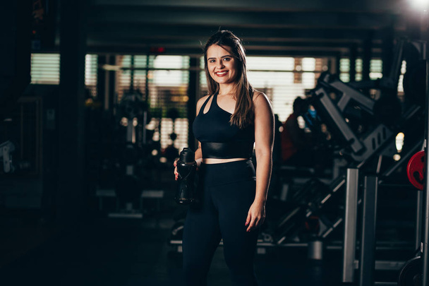 A young woman taking a break at the gym with a bottle of water or energy drink - Foto, immagini