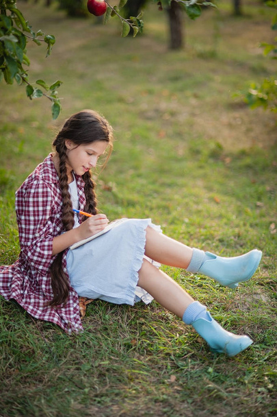 The girl sitting under the tree and wrote in Notepad - Photo, Image
