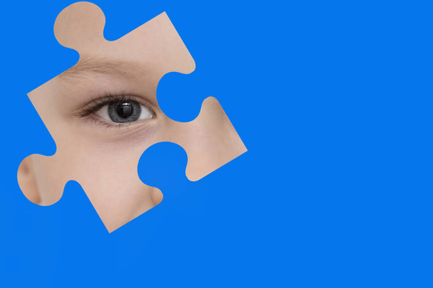 Kind spioniert durch ein blaues Puzzle. Symbol des Autismus-Bewusstseins - Foto, Bild