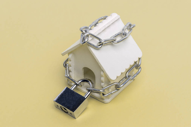 Παιχνίδι σπίτι τυλιγμένο με μια αλυσίδα με ένα μεγάλο κλείδωμα σε κίτρινο φόντο ως σύμβολο της εγγυημένης ασφάλισης - Φωτογραφία, εικόνα
