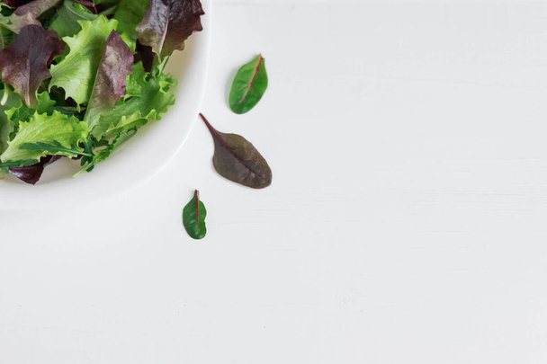 Plate with lettuce on a white wooden background. Salad greens. Organic food. Food For Vegans. Design a banner with natural food. Salad to lose weight. Flat lay, top view. - 写真・画像