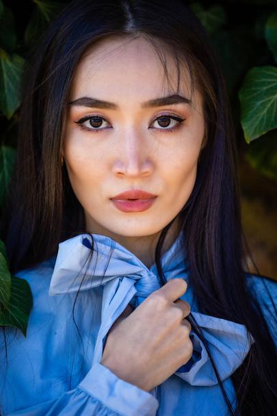 Portret van de jonge stijlvolle Aziatische vrouw in groene bladeren op muur achtergrond - Foto, afbeelding