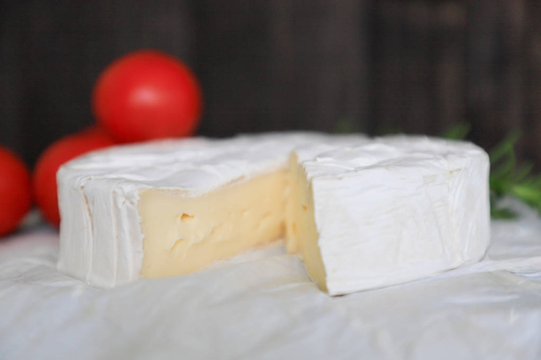 Egész Brie sajt fehér kézműves papíron, a háttérben piros paradicsom és fa háttér - Fotó, kép