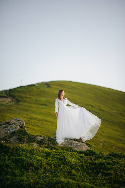 woman in a wedding dress runs across the field toward the mountains - Fotografie, Obrázek