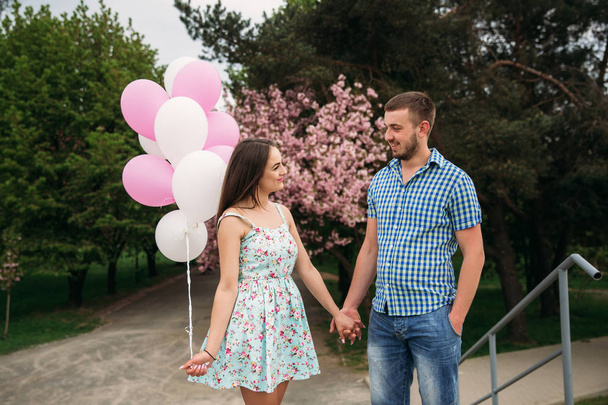 Young happy couple in love outdoors. Handsome man and beautiful woman on a walk in a spring blooming park. They keep helium balls - Foto, Imagem