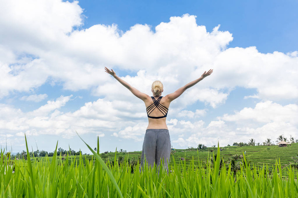 Relaxado mulher desportiva saudável, braços erguidos para o céu, desfrutando de natureza pura em belos campos de arroz verde em Bali
. - Foto, Imagem