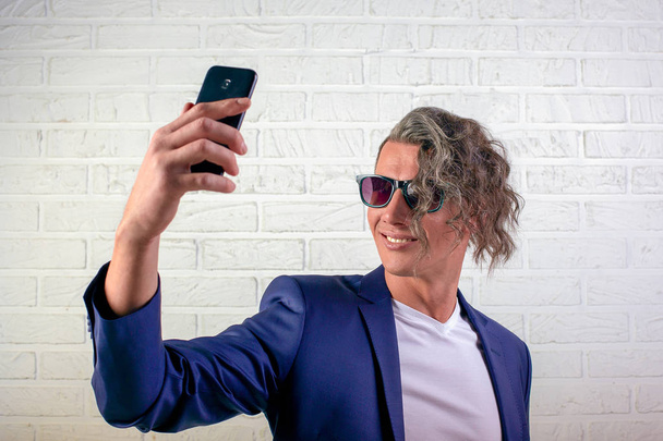 διαχειριστής ή επιχειρηματία με κομψά σγουρά μαλλιά σε λευκό t-shirt σε άσπρο φόντο κάνει selfie στο κινητό τηλέφωνο, συνομιλία και πληροφορίες - Φωτογραφία, εικόνα