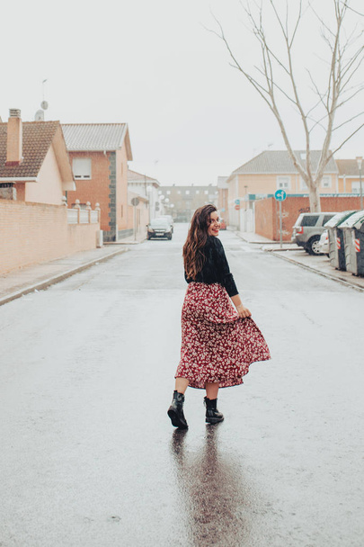 Young girl wetting her skirt and smiling in the rain with black boots and printed long skirt - Фото, изображение