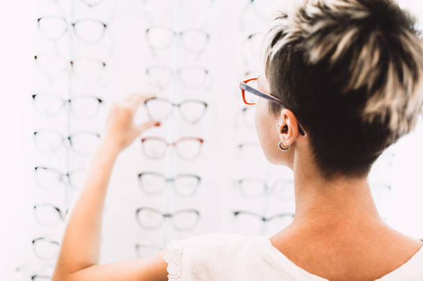 Beautiful middle age woman choosing a glasses in optician store. - Fotografie, Obrázek