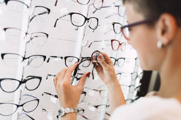 Beautiful middle age woman choosing a glasses in optician store. - Valokuva, kuva