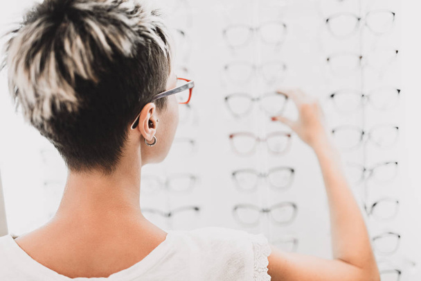 Beautiful middle age woman choosing a glasses in optician store. - Fotoğraf, Görsel