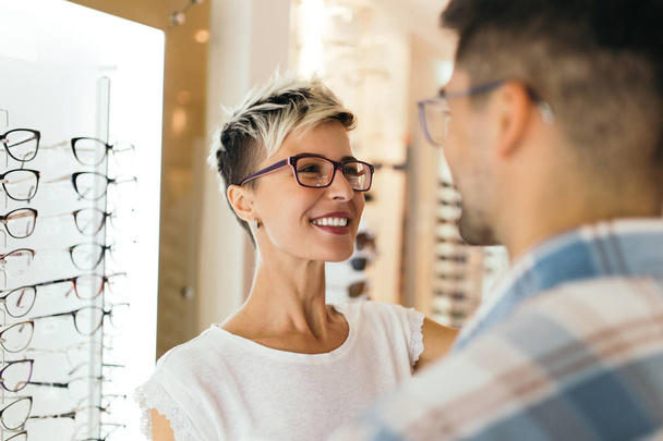 Attractive young couple in optical store buying glasses and smiling - Фото, зображення