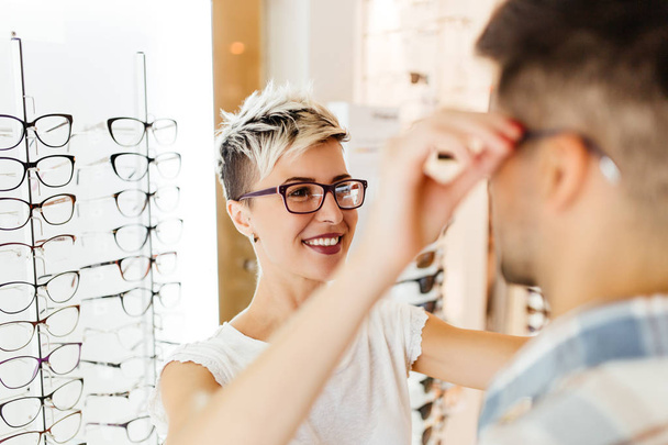 Attractive young couple in optical store buying glasses and smiling - Foto, Imagem