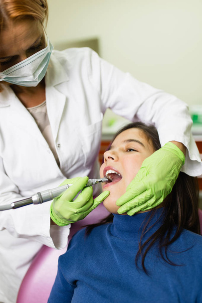 Cute little school girl sitting on dental chair while having dental treatment. Close up shot. Selective focus. Dental health concept. - Photo, Image
