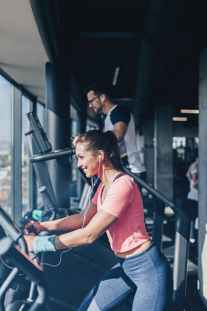 Young fit man and woman running on treadmill in modern fitness gym. - Fotografie, Obrázek