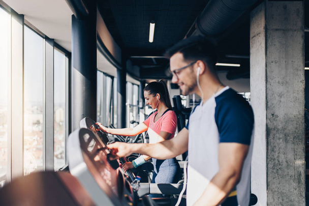 Young fit man and woman running on treadmill in modern fitness gym. - Foto, immagini