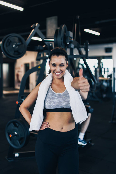 Young attractive woman after successful workout posing and smiling in modern fitness gym while showing thumb up - Valokuva, kuva