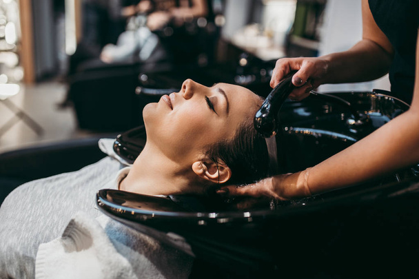 Beautiful young woman getting a hair wash. Hair salon styling concept. - 写真・画像