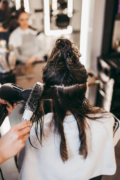 Beautiful brunette woman with long hair at the beauty salon getting a hair blowing. Hair salon styling concept. - Photo, image