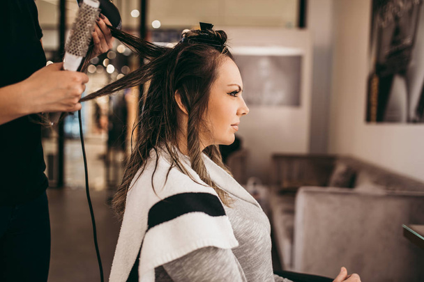 Beautiful brunette woman with long hair at the beauty salon getting a hair blowing. Hair salon styling concept. - Foto, Imagem