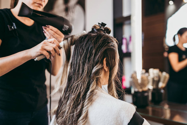 Beautiful brunette woman with long hair at the beauty salon getting a hair blowing. Hair salon styling concept. - Foto, imagen