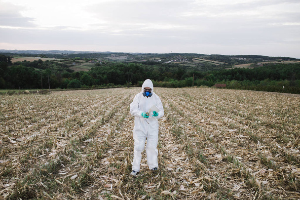 Weed control. Industrial agriculture researching. Man with digital tablet in protective suite and mask taking weed samples in the field. Natural hard light on sunny day.  - Φωτογραφία, εικόνα