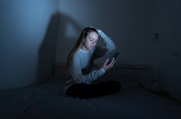 Sad desperate young teenager female girl on smart phone suffering from online bulling and harassment felling lonely and hopeless sitting on bed at night. CYberbullying and dangers of internet concept. - Фото, зображення