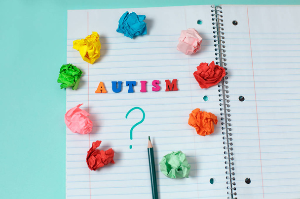 AUTISM colorful word from color wooden letters on notebook page and question mark with a pencil surrounded by crumpled colored papers. Concept image - Photo, Image