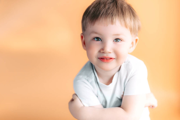 Portrait of blonde happy joyful beautiful cute little boy looking at camera on orange background - Фото, изображение