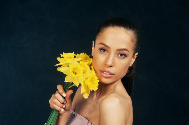 Πορτρέτο του ένα νεαρό όμορφο κορίτσι με τα λουλούδια στο στούντιο. Η έννοια της γυναικείας ομορφιάς και της ελκυστικότητας - Φωτογραφία, εικόνα