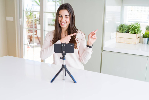 Bella giovane donna che registra video selfie con webcam smartphone sorridente e guardando la fotocamera che punta con due mani e dita lateralmente
. - Foto, immagini