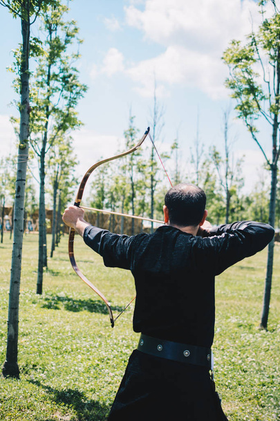 Bogenschütze in traditioneller Kleidung schießt einen Pfeil - Foto, Bild