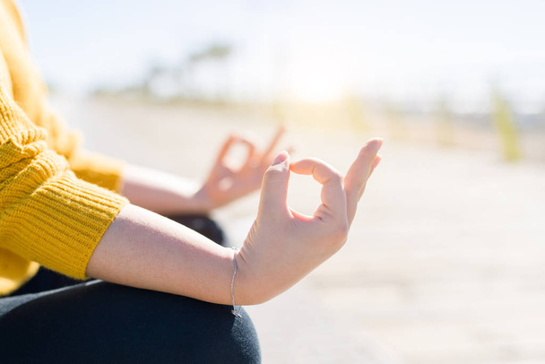 schöne junge Frau sitzt auf einer Promenade am Meer und macht Yoga-Pose, meditiert, genießt Sonnenlicht und entspannt sich an sonnigen Tagen - Foto, Bild