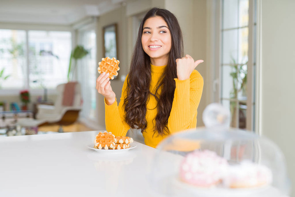Молода жінка їсть солодке вафельне тісто, вказуючи і показуючи з великим пальцем в сторону з щасливим обличчям посміхаючись
 - Фото, зображення