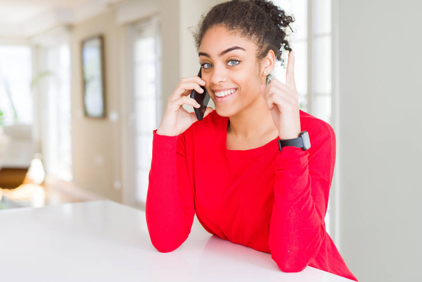 Young african american woman having a conversation talking on smartphone surprised with an idea or question pointing finger with happy face, number one - Foto, afbeelding