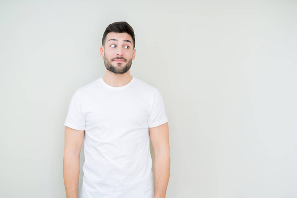 Mladý pohledný muž nosí ležérní bílé tričko izolované pozadí vypadající strana a vytřeštěné pryč myšlení. - Fotografie, Obrázek