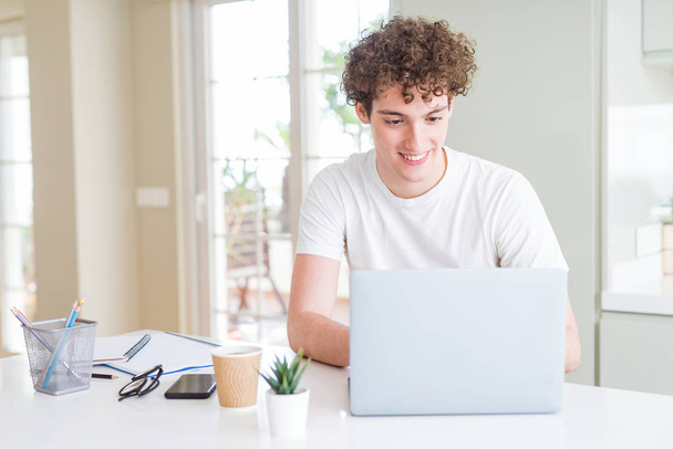 Молодой студент работает и учится с помощью компьютера ноутбука с счастливым лицом стоя и улыбаясь с уверенной улыбкой показывая зубы
 - Фото, изображение